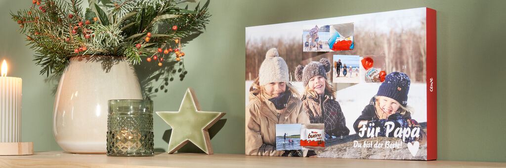 Auf einem Sidebord steht ein Adventskalender neben einem weihnachtlichen Gesteck und einer Kerze. Der Adventskalender hat vorne ein Foto von drei Kindern mit der Aufschrift "Für Papa". Drei der Türchen sind geöffnet, dahinter befindet sich kinder® Schokolade. Die Innenseiten der drei Türchen zeigen Fotos von den Kindern und dem Vater.