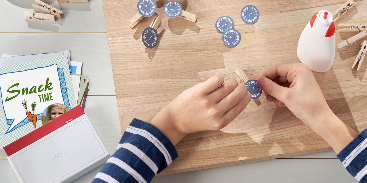 Person bastelt mit Wäscheklammern und Papierstücken auf einem Holztisch, um kreative Ideen zu gestalten.