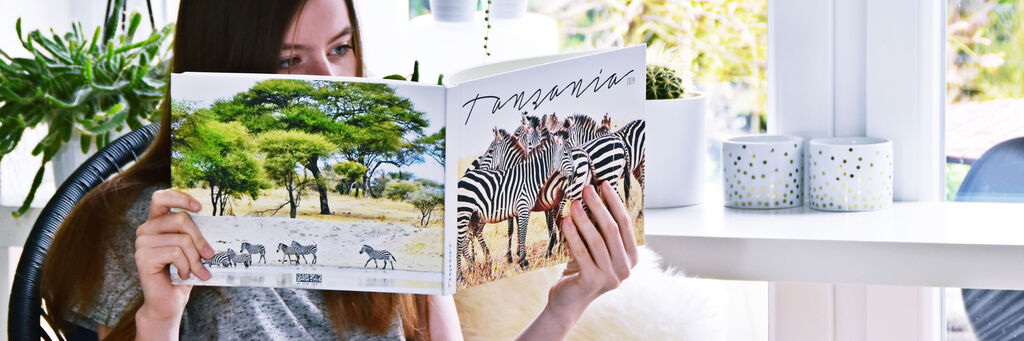 Nics Tochter hält das Fotobuch zur Afrika-Reise aufgeschlagen in ihren Händen. Auf beiden Seiten sind Fotos von Giraffen zu sehen.